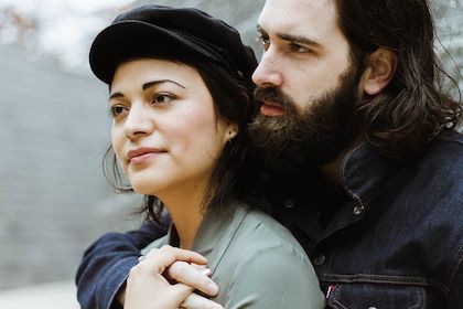 A couple holding one another, looking over one shoulder together. 