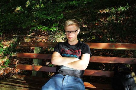 Young male sitting on a bench with his arms crossed, expressing rejection. 