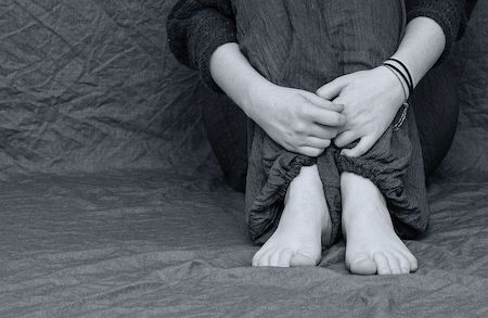 Black and white photo of person sitting and holding themselves. 