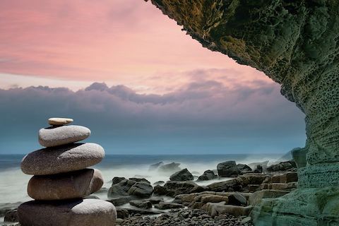 View of a cliff with an ocean sunset in the background, neatly stacked rocks are the focal point. 