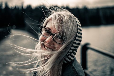 Woman with glasses smiling, the breeze is blowing her hair about. 