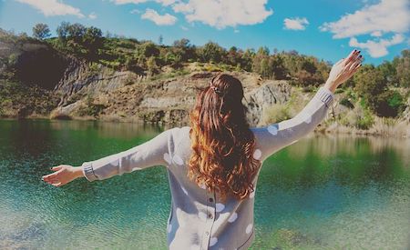 Rear view of a woman holding her arms out in front of a beautiful lake, expressing freedom. 