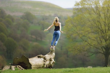 Woman jumping off of a fallen tree trunk, expressing spiritual freedom. 