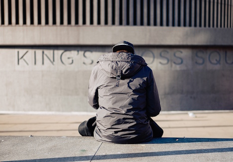 Rear view of a man sitting on a bench in front of a concrete building. 