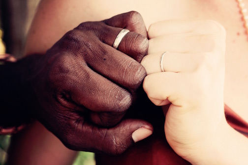 Interracial couple holding their hands together showing their wedding bands. 