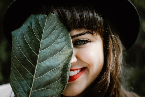 Woman smiling but covering half of her face with a large leaf. 