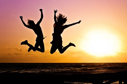 A silhouette of two woman jumping in joy, there is a sunset in the background. 