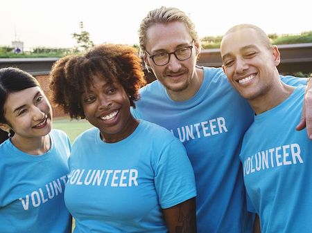 Group of 4 friends smiling, they are all wearing blue t shirts that say volunteer. 