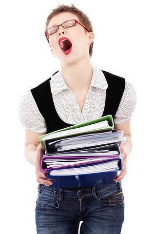 Short haired woman with glasses making a yelling gesture while holding a stack of books, expressing a stressed state. 