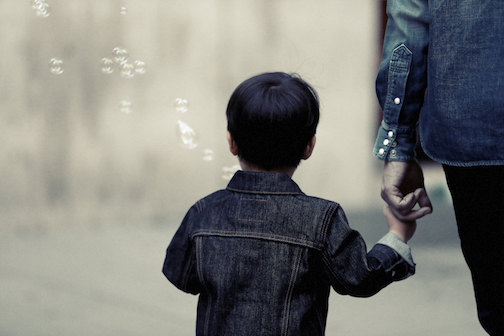 Mother and son walking and holding hands, the child is blowing bubbles. 