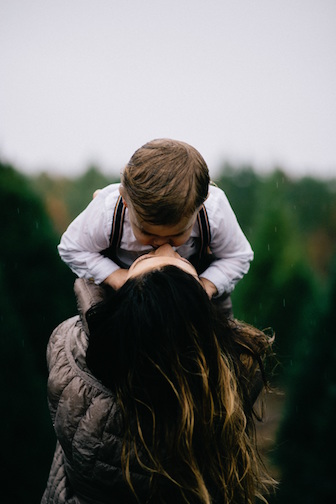 A mother holding up her little boy and kissing him on the face. 