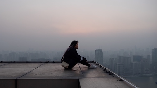 Person looking onward to the city as they sit on a rooftop. 