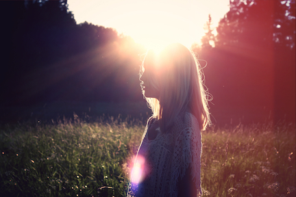 A silhouette of a woman in a field, the sun is creating the silhouette. 