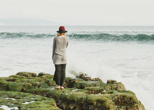 Woman standing on a rocky beach viewing the surf. 