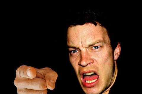 Close up of a man yelling and pointing into the camera with a black background.