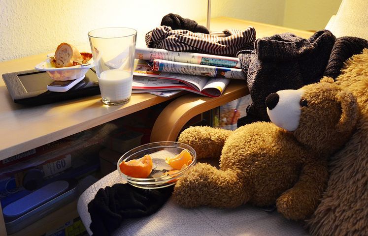 A cluttered desk with clothes, books, half drank milk, etc. 