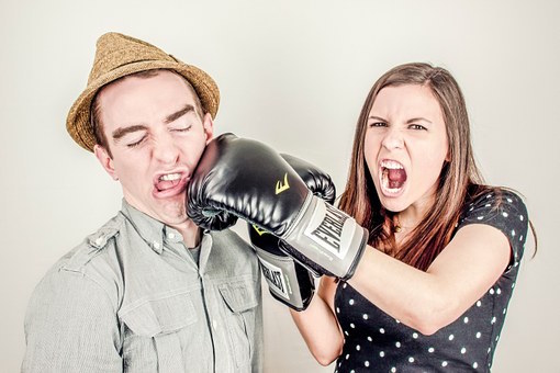A couple illustrating conflict, the woman is screaming and punching the man in the face with a boxing glove on. 