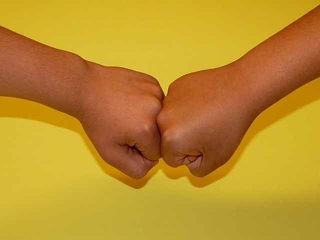 A close up of two kids fist bumping with a yellow background. 