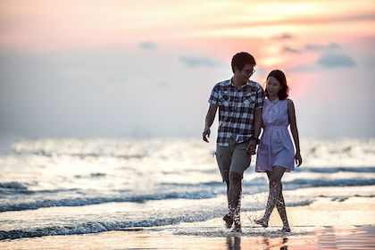 Couple holding hands walking on beach.