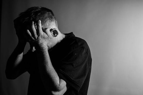 Black and white picture of a man holding his head in his hands, expressing stress and pain.