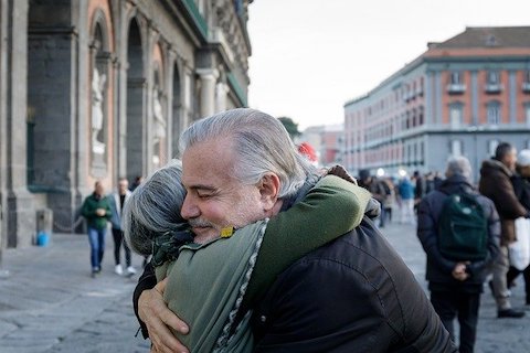 Two older people embracing each other with a hug in a downtown area. 