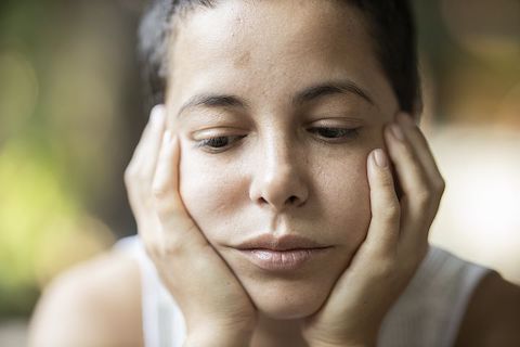 Close up of a woman holding her face in her hands, looking depressed. 