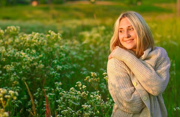 A woman in a field of flowers hugging herself and smiling. 
