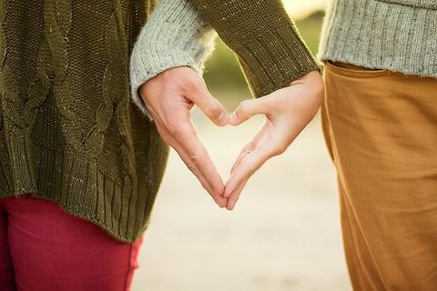 Close up of two people making a heart with their adjoined hands. 