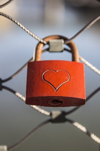 Red padlock with heart etched onto it, locked on a chain link fence. 