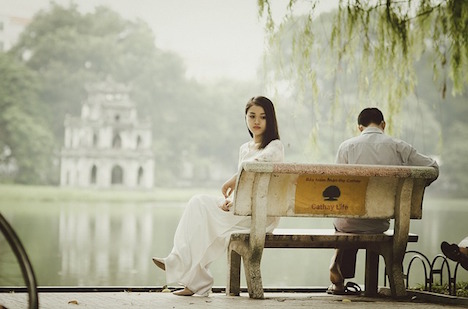 A couple facing back to back on a park bench. 