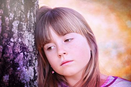 Young woman resting her head beside a tree, expressing loneliness. 