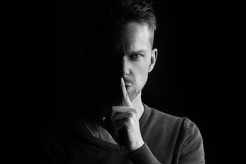 Black and white photo of a man gesturing to shush. 