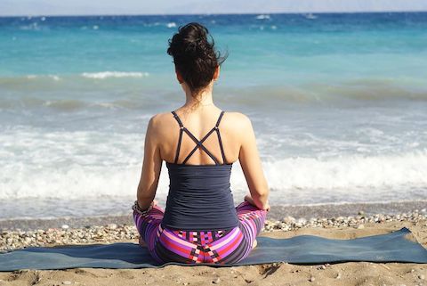 Woman sitting on a yoga mat and practicing meditation on a beach. 
