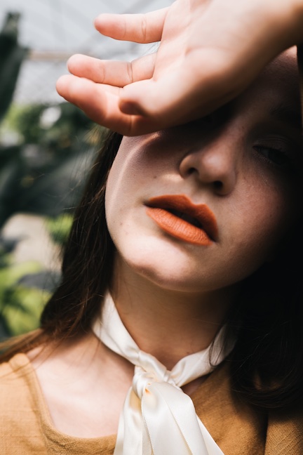 Close up view of a female face, she is holding the back of her hand on her forehead expressing fatigue. 