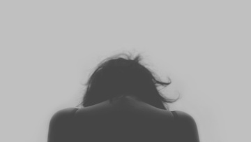 Black and white rear view of a woman sulking with her head down. 