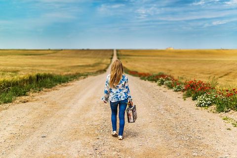 Woman walking alone with a small briefcase on a rural, dirt road. 