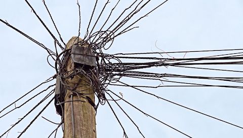 Close up and upward view of telephone pole with a disorganized cluster of wires. 