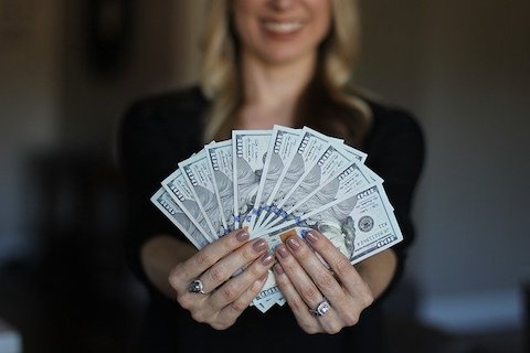 Woman showcasing her multiple, hundred dollar bills while smiling. 