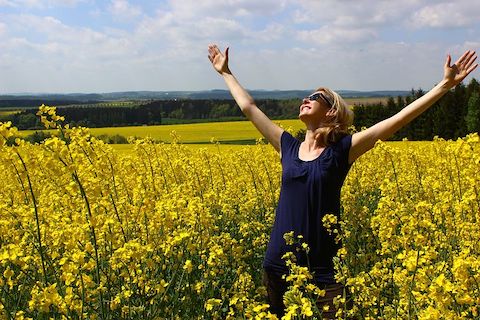 Woman in a sundress smiling and embracing the sky with open arms, in a field of yellow flowers. 