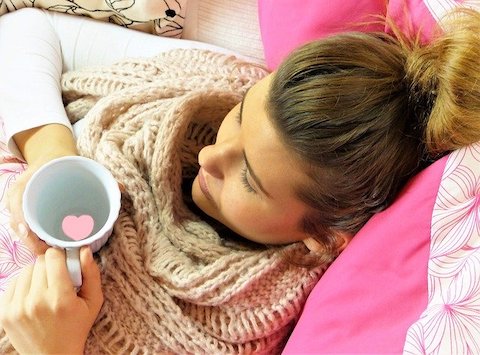 Young woman comfortably relaxing on her back holding a coffee cup near her face. 